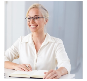 Eine Frau mit breitem Grinsen sitzt an einem Tisch und hält einen Stift in der Hand.